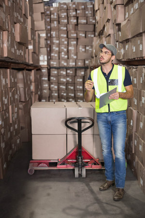 Male warehouse worker scanning pallet jack with tablet and stylus in warehouse aisle, copy space....