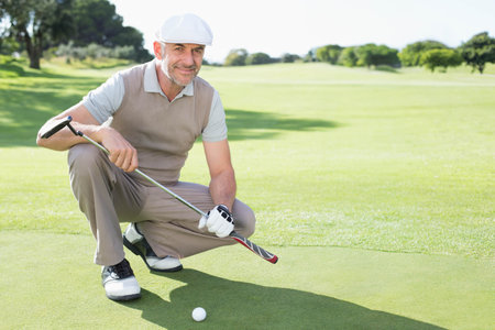 Senior male golfer in golf attire lining up putt on putting green with golf ball. Athletic, leisure, outdoor, precision, activity, sport, relaxationの写真素材