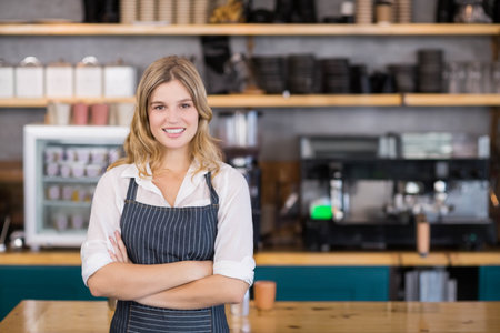 Female barista standing behind coffee bar wearing apron and posing by espresso machine in cafe....