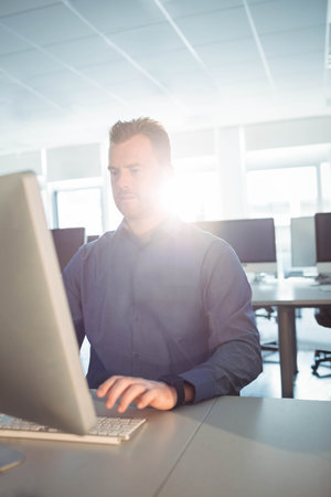Monitor glowing on open-plan office desk under sunlight streaming through windows, copy space....