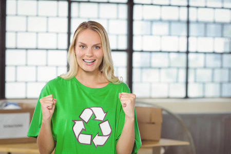 Smiling adult female wearing green recycling T-shirt standing in warehouse sorting cardboard boxes. Environmentalist, sustainability, eco-friendly, volunteer, activity, workshop, vibrantの写真素材