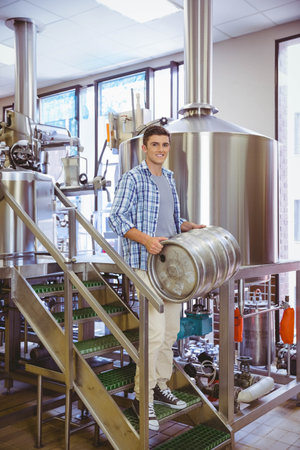 Stainless steel keg resting on grated stairway inside brewery production area, with polished tanks....