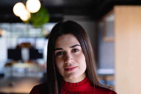 Woman working in open-plan office wearing red blouse among desks computer monitors and plant. Professional, corporate, modern, minimalist, productivity, work environment, businessの写真素材