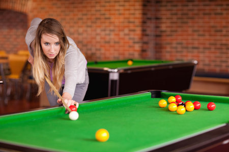 Woman leaning over pool table in pool hall, aiming white ball with cue stick, copy space....