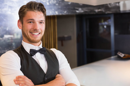 male bartender in black vest smiling and standing at lounge bar counter with bag, copy space....