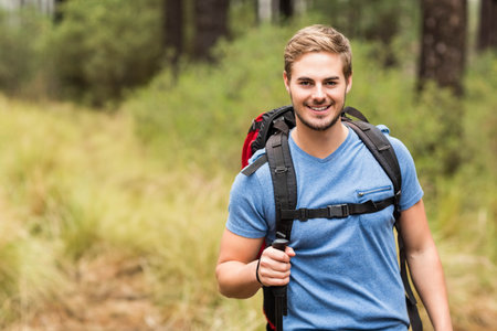 Man in his twenties walking on forest path wearing blue t-shirt carrying backpack, copy space. Adventure, exploration, nature, wilderness, outdoors, vitality, healthの写真素材