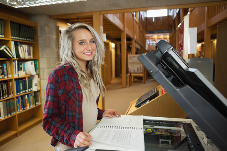 Female student wearing flannel shirt preparing spiral-bound document at library scanner, copy space....