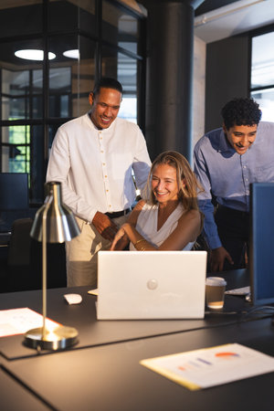 Colleagues collaborating on laptop in modern office, smiling and discussing project. Teamwork, collaboration, business, corporate, brainstorming, discussionの写真素材