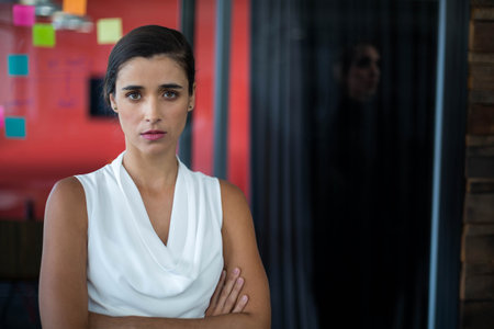 Woman standing in office room surveying sticky notes on red accent wall through glass partition. Collaboration, planning, innovation, modernity, productivity, brainstorming, workspaceの写真素材