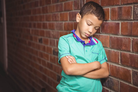 Schoolboy leaning against brick corridor wearing polo with collar stripes, copy space. Youth, urban, textured, contemplative, casual, moody, architectureの写真素材