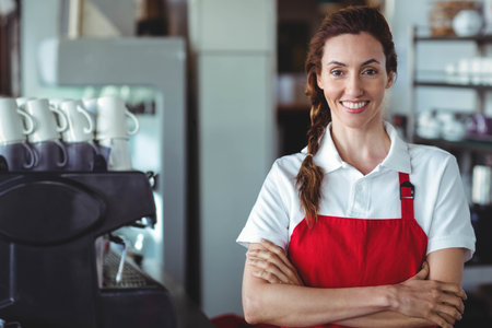 Female barista wearing red apron and smiling at counter with espresso machine, copy space....