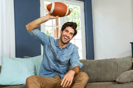 Football hovering above gray sofa in living room, with light filtering through glass door. Casual, relaxation, modern, interior, leisure, comfort, masculineの写真素材