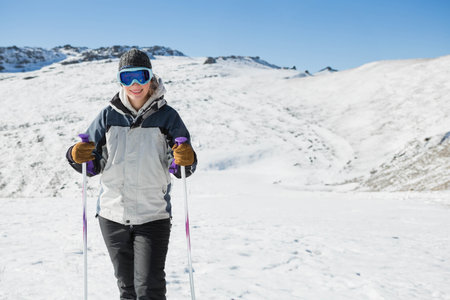 Skier standing on snowfield at mountain base under clear blue sky holding purple poles, copy space. Adventure, winter, alpine, outdoor, activity, landscape, explorationの写真素材