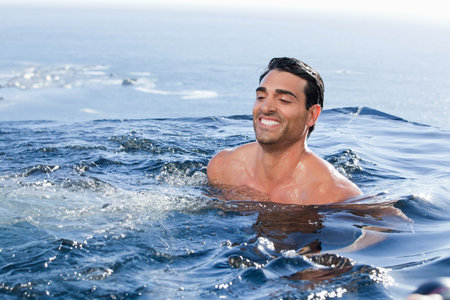 Mid adult shirtless man smiling in sea waves under clear sky with sunlight reflections, copy space. Marine, wellness, vitality, tranquility, outdoor, adventure, reflectionの写真素材