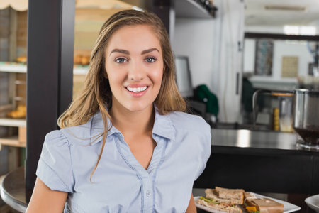 Smiling female barista preparing sandwich on metal counter beside espresso machine. Cafe, hospitality, artisan, cozy, pastry, latte, casualの写真素材