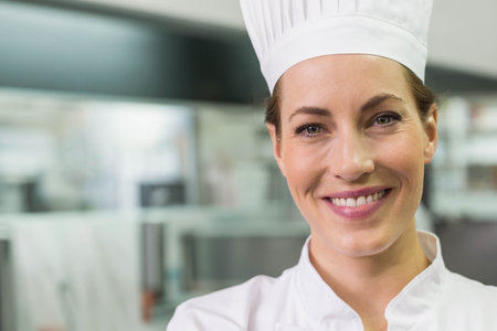 Female chef standing in commercial kitchen with counters wearing chef hat and jacket, copy space. Professional, culinary, gourmet, modern, industrial, hygiene, craftsmanshipの写真素材