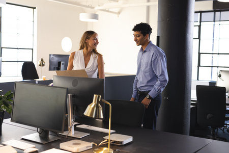 Colleagues discussing project in modern office, smiling and holding documents. Collaboration,...