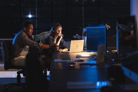 Colleagues collaborating on laptop in modern office during late-night work session. Teamwork, collaboration, business, corporate, productivity, brainstormingの写真素材