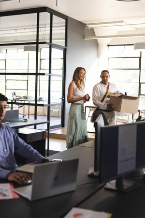 Colleagues welcoming new employee carrying box into modern office workspace. Teamwork, onboarding, collaboration, teamwork, coworkers, diversityの写真素材