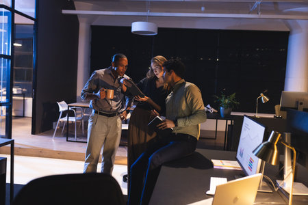 Business professionals discussing project details in modern office during late hours. Collaboration,...