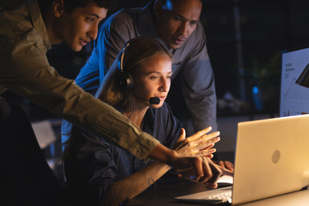 Team collaborating at night, focused on laptop screen, discussing project details. Teamwork,...