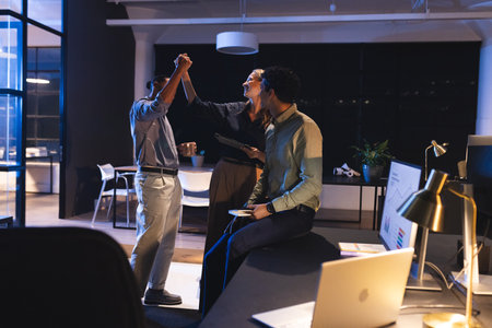 Celebrating success, diverse colleagues high-fiving in modern office at night. Teamwork, diversity,...