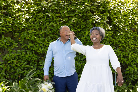 Senior couple dancing joyfully in garden, holding hands and smiling brightly. Elderly, happiness, celebration, romance, outdoor, leisureの写真素材