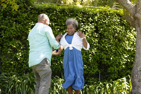 Senior couple enjoying playful moment together in lush green garden outdoors. Elderly, greenery, happinessの写真素材