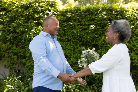 Senior African American couple holding hands and smiling in garden with flowers. Elderly, relationship, nature, gardening, happiness, loveの写真素材