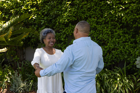 Senior couple dancing joyfully in garden, surrounded by lush greenery. Elderly, lifestyle, gardening, happy, nature, leisureの写真素材