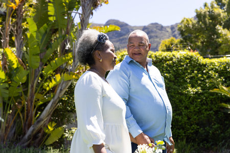 African American senior couple walking in garden, enjoying sunny day together. Elderly, wellness, leisure, bonding, outdoors, relaxationの写真素材