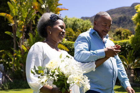 Senior African American couple walking in garden, holding hands and smiling joyfully. Togetherness, bonding, gardening, nature, happiness, elderlyの写真素材