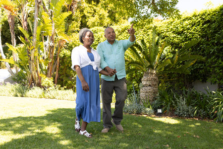 Senior couple walking in garden, enjoying sunny day and nature together. Retirement, leisure, companionship, outdoors, wellnessの写真素材