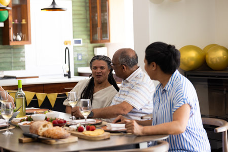 Senior friends enjoying conversation and wine at home during festive gathering. Celebration, friendship, togetherness, leisure, bonding, socializingの写真素材