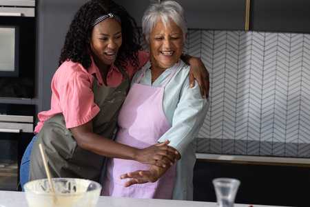 Grandmother and granddaughter laughing together while baking in modern kitchen. Family, bonding, happiness, activity, home, multigenerationalの写真素材
