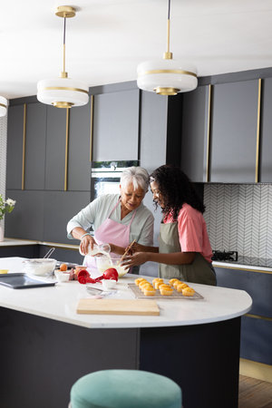 Baking together in kitchen, grandmother and granddaughter sharing joyful moment. Family, bonding, generations, fun, cooking, relationshipの写真素材