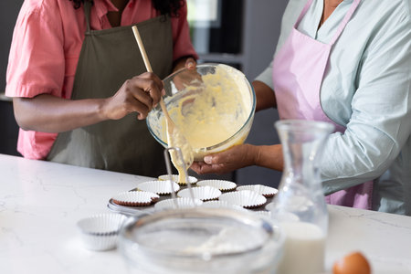 African American family baking cupcakes together in kitchen, enjoying quality time. bonding, cooking, parenthood, teamwork, dessert, togethernessの写真素材