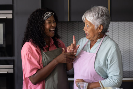 African American woman and elderly woman laughing together in kitchen while cooking. laughter, friendship, bonding, diversity, happiness, multi-generationalの写真素材