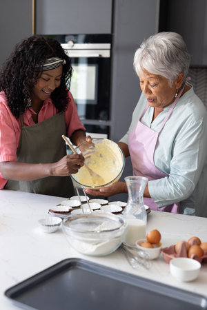 Baking cupcakes, African American woman and elderly woman smiling warmly in kitchen. family bonding, preparing, culinary, dessert, grandmother, homemadeの写真素材