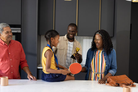 Family celebrating young girl's achievement with trophy and table tennis paddle. Celebration, awards, joy, success, sportsの写真素材
