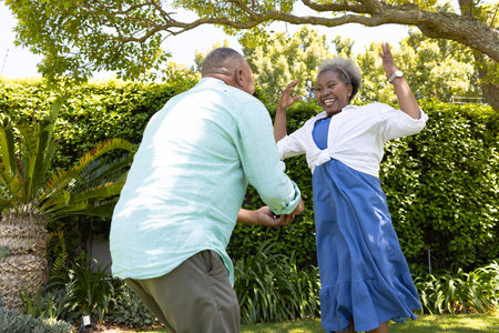 Senior couple dancing joyfully in garden, enjoying sunny day together. Elderly, happiness, love, outdoors, lifestyle, togethernessの写真素材