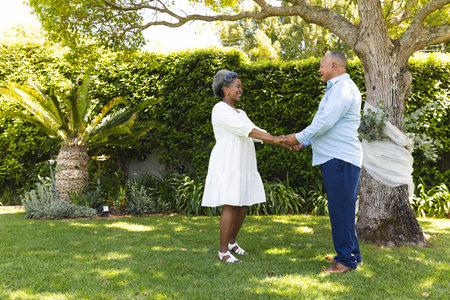 Senior couple holding hands in garden, smiling and enjoying sunny day together. Elderly, companionship, gardening, happiness, bonding, outdoorsの写真素材