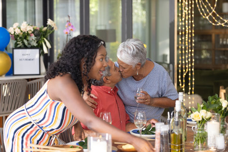 Celebrating retirement, African American family sharing festive meal and affection. celebration, family gathering, joy, togetherness, happiness, affectionateの写真素材