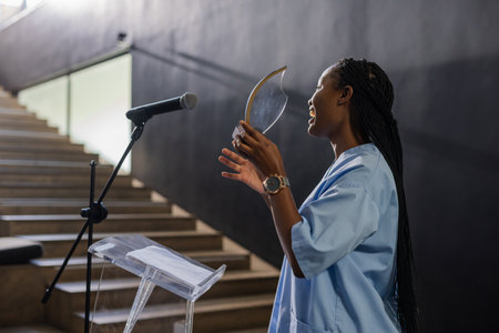 African American woman holding award plaque and speaking at podium in auditorium, copy space. Presentation, leadership, recognition, empowerment, professionalism, healthcare, conferenceの写真素材
