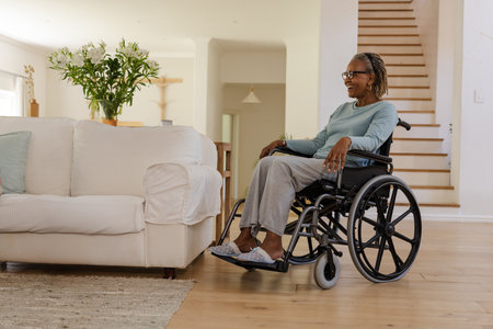 Senior African American woman sitting in wheelchair in living room, with flower vase, copy space....