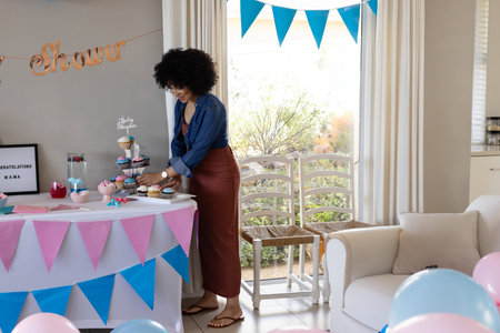 African American woman arranging cupcakes on cupcake stand in living room with bunting, copy space....