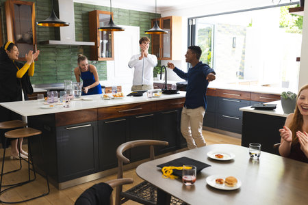 Teens celebrating in modern kitchen, laughing and clapping during joyful gathering. Celebration, friendship, happiness, diversity, youth, socializingの写真素材