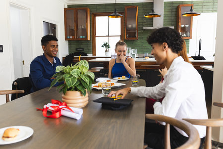 Teens celebrating graduation at home, enjoying food and laughter around table. celebration,...