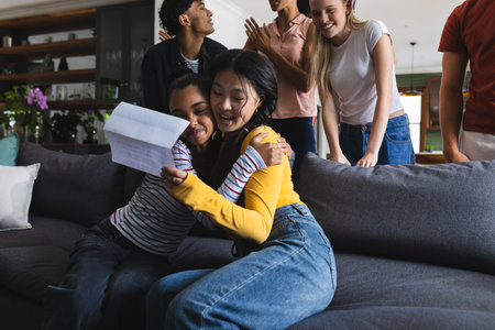 Teen friends celebrating good news at home, hugging and smiling with excitement. Friendship, celebration, happiness, joy, emotion, bondingの写真素材