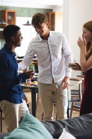Teen friends laughing and enjoying drinks at home during celebration. Party, friendship, beverages, laughter, socializing, funの写真素材